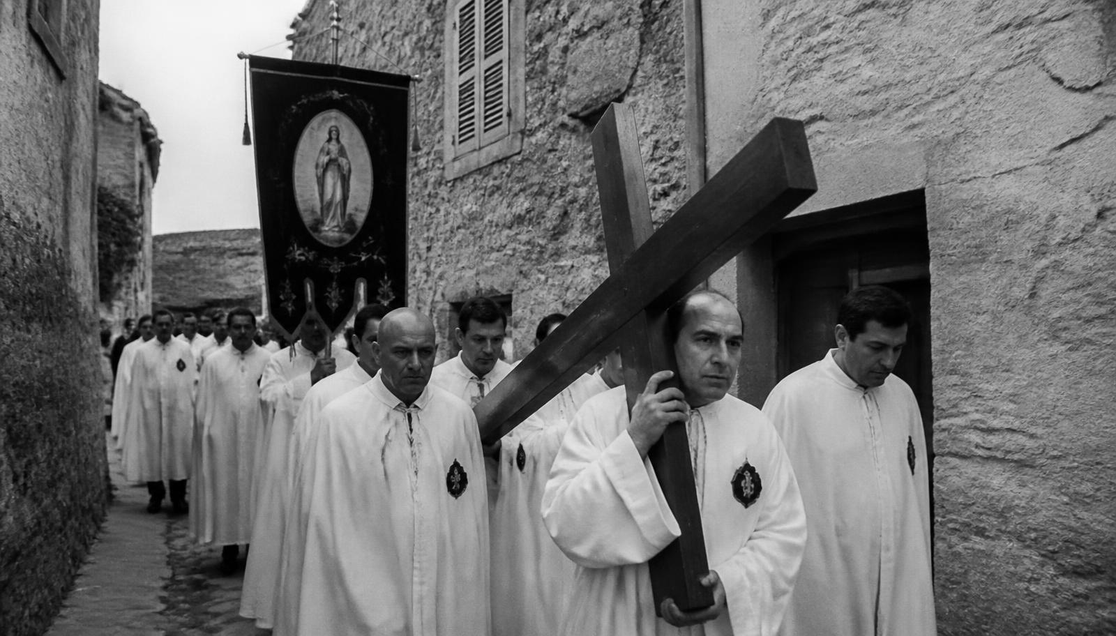 Procession de la confrérie San Francescu dans une ruelle de village, hommes en aube blanche portant la croix
